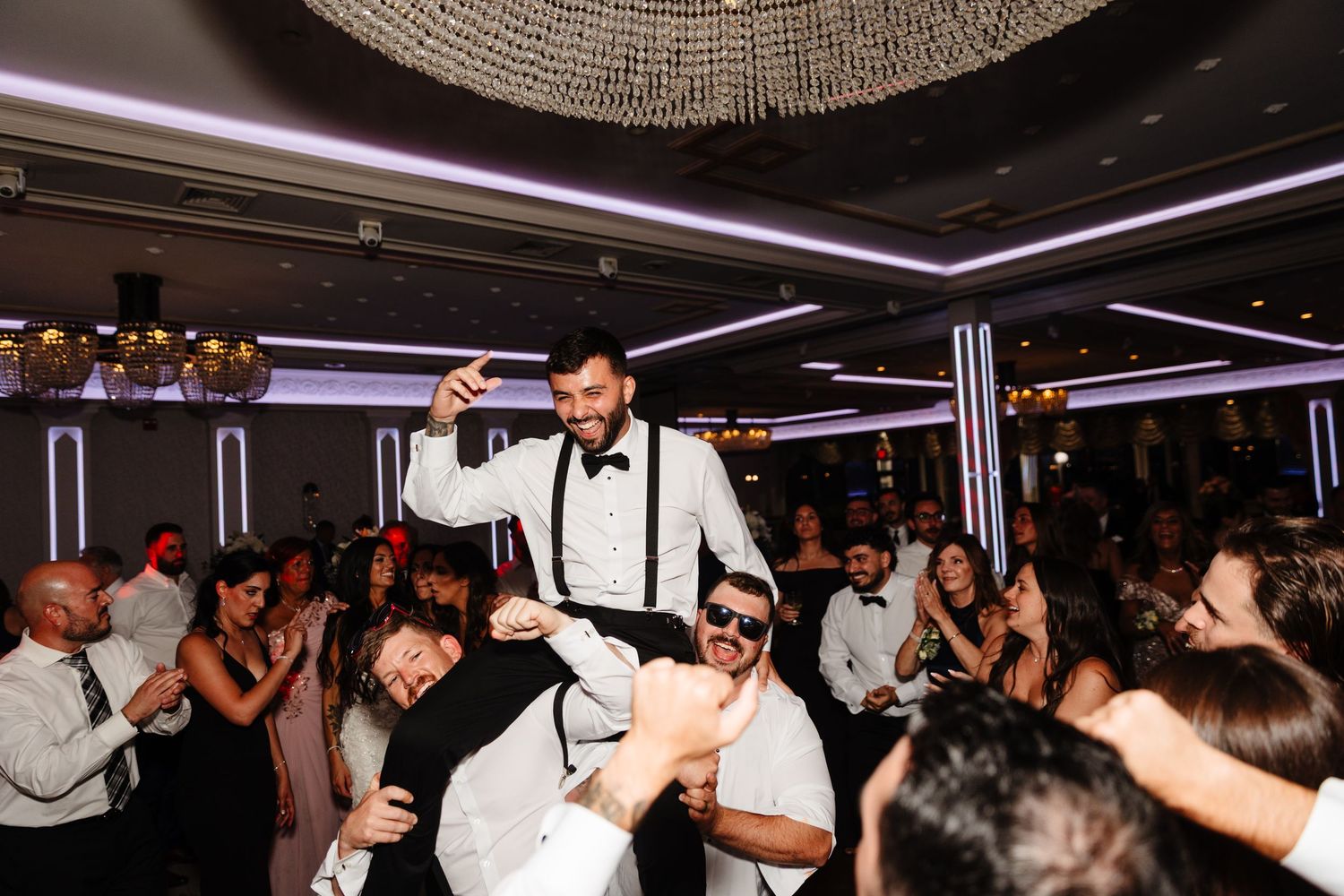 Wedding guests hoist the groom up during an energetic reception dance party.