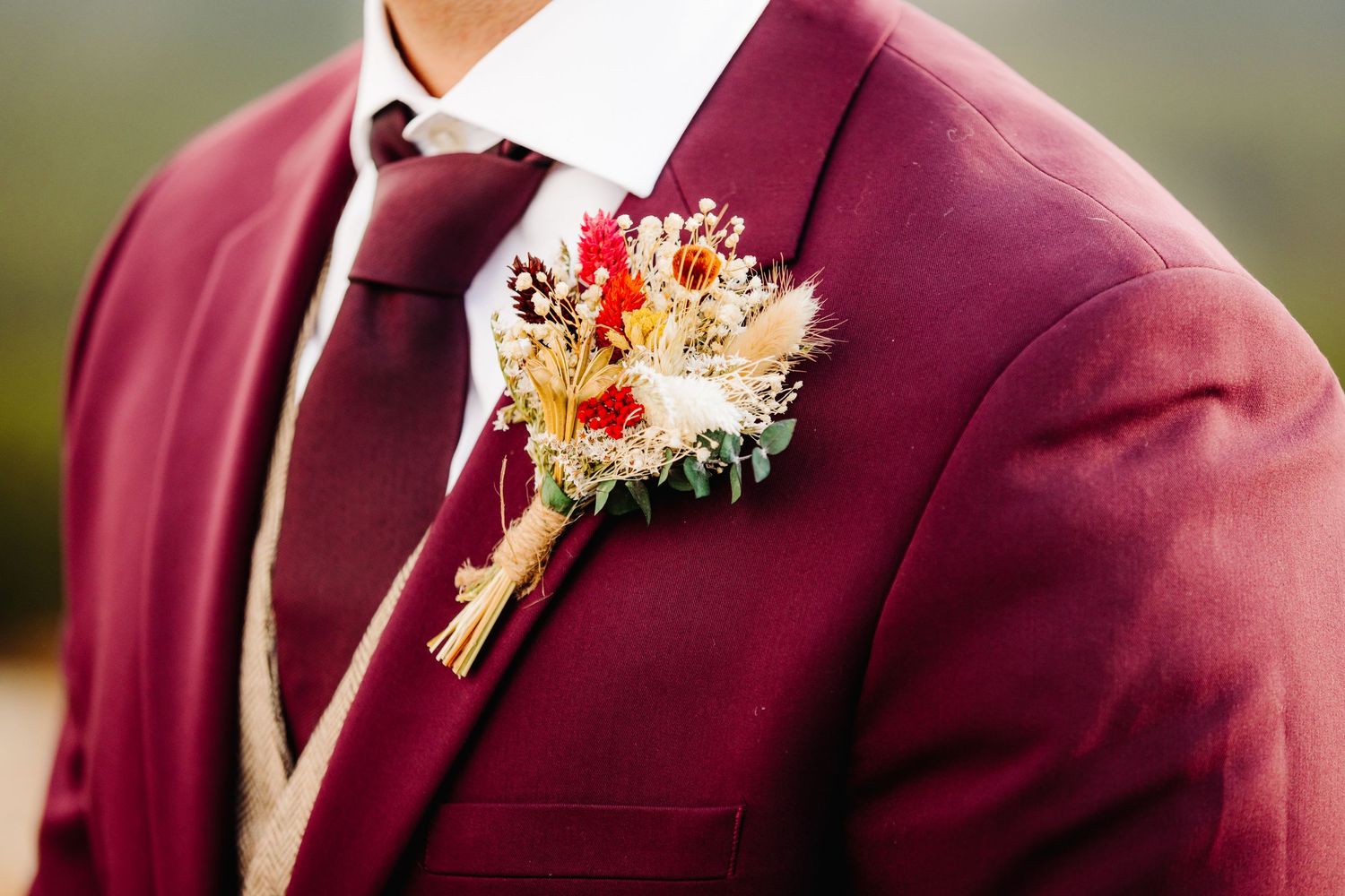 Detail shot of burgundy suit lapel with delicate floral boutonniere.