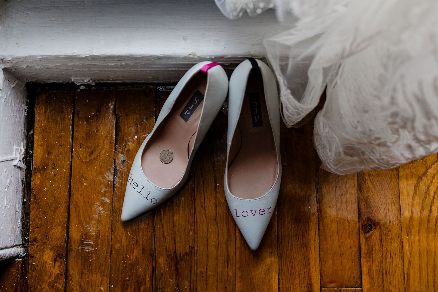 Pale blue wedding shoes placed on wooden flooring next to flowing white tulle.