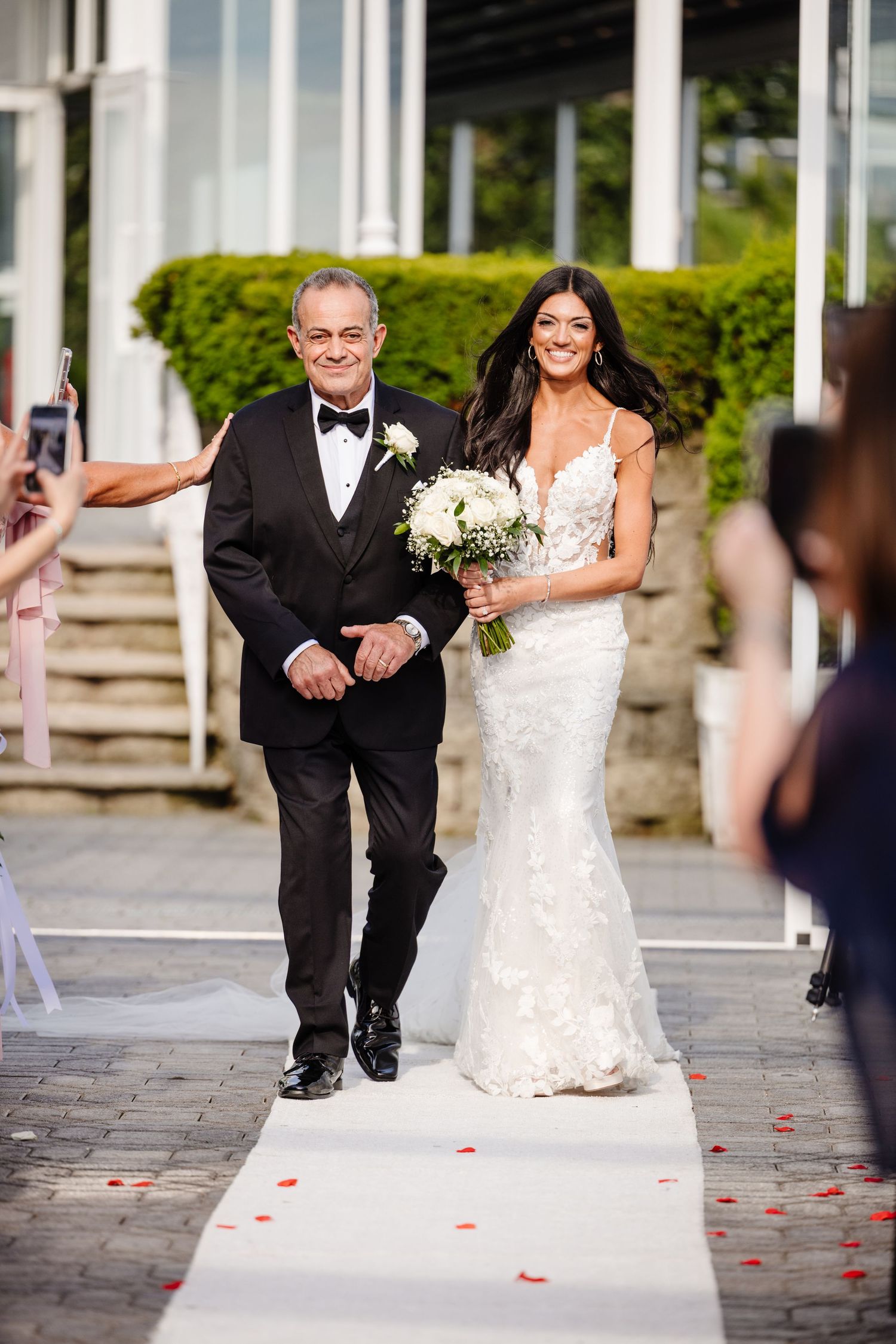 Wedding couple walks down an elegant stone pathway with rose petals scattered.