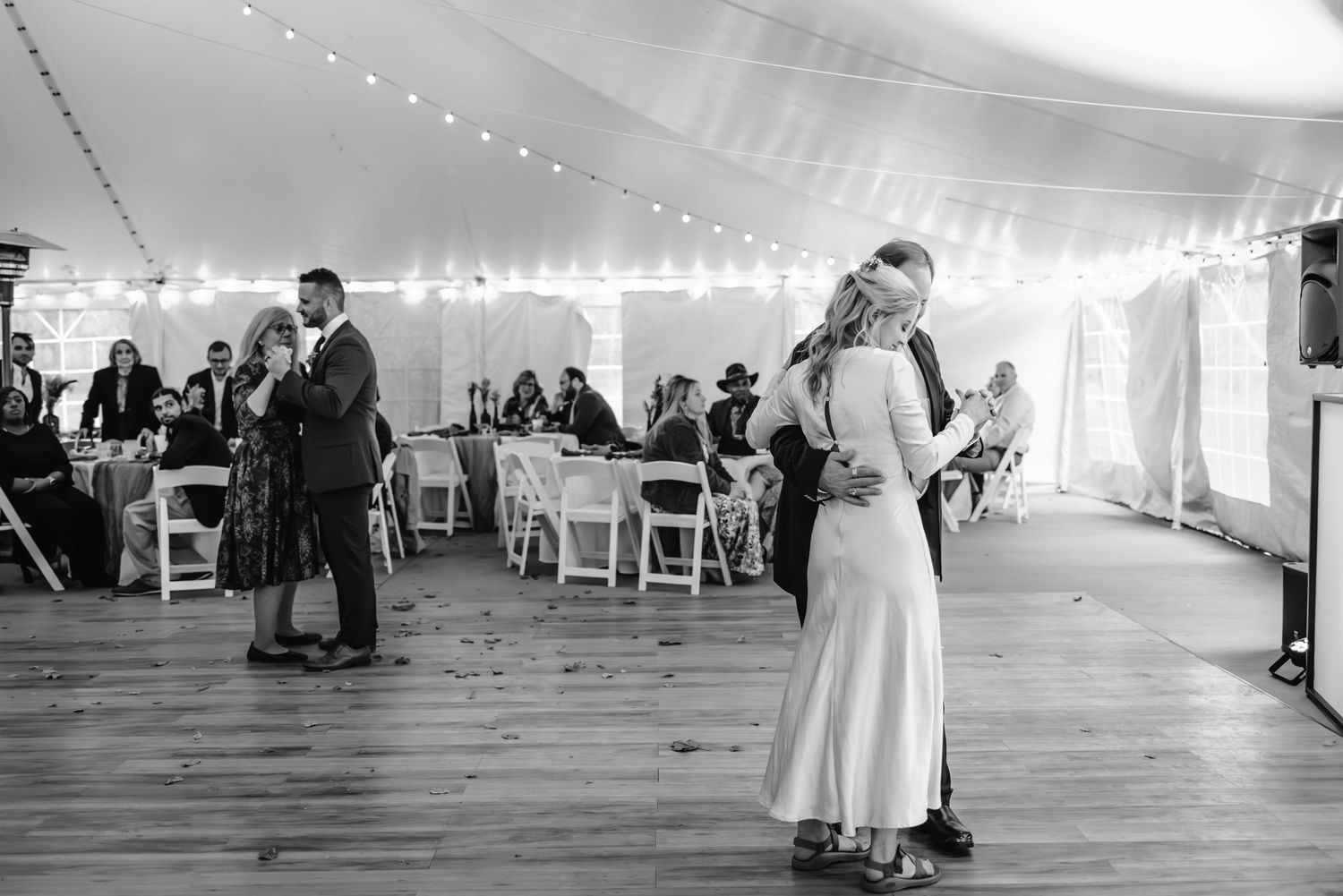 Couples slow dancing on wooden floor under tent at evening wedding reception.