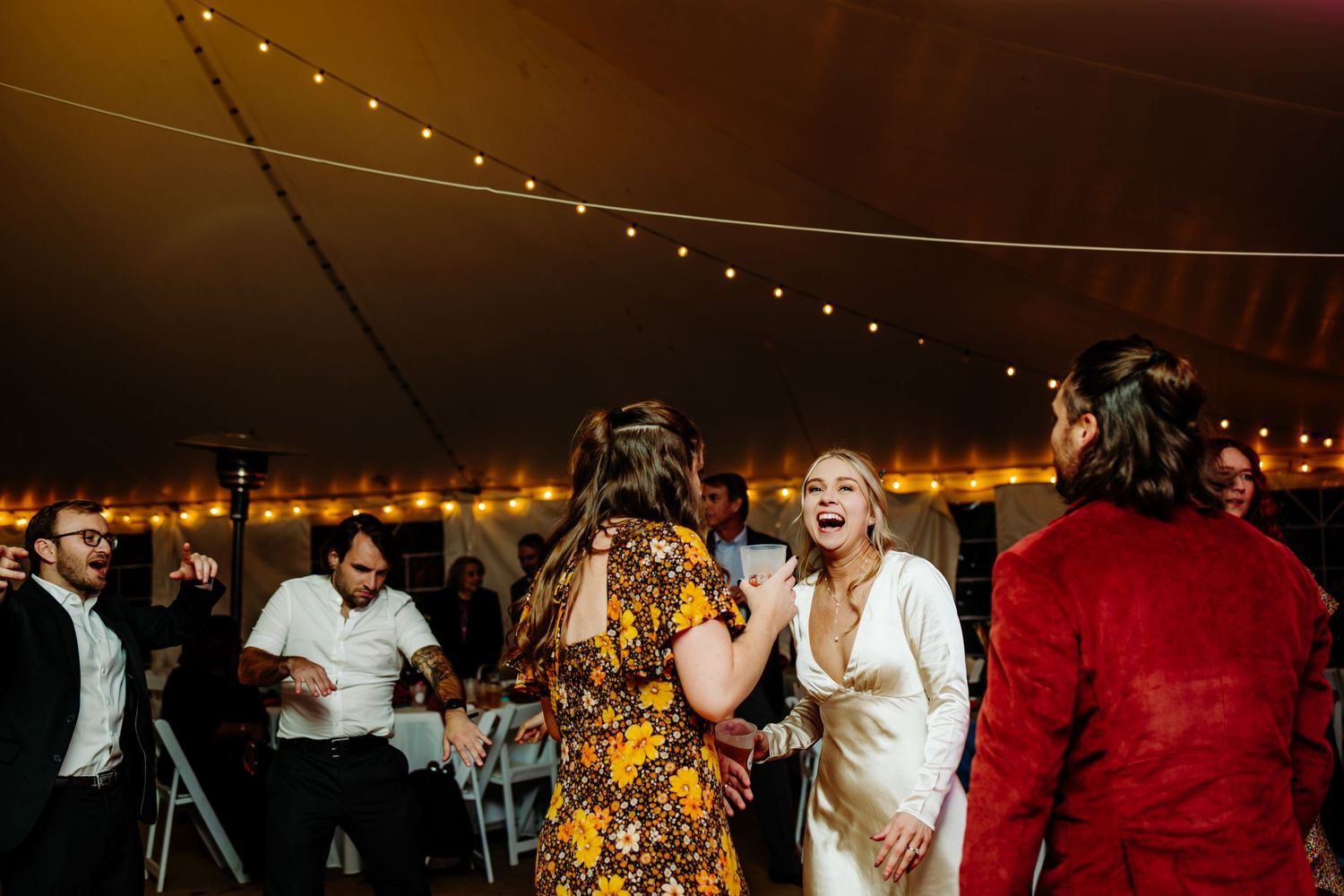 Wedding reception party with guests dancing under string lights in tent venue.