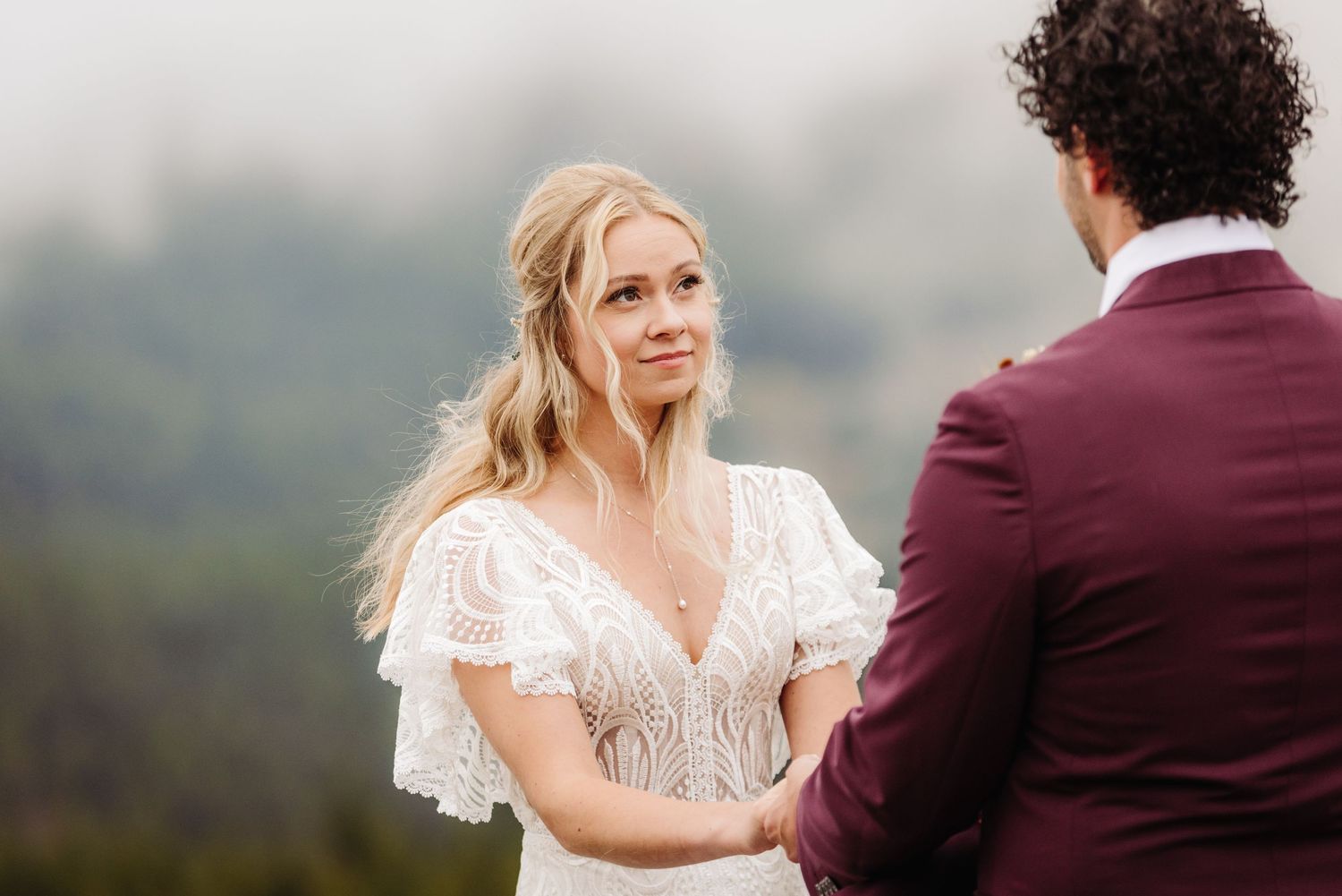 Intimate wedding ceremony moment against misty mountain landscape backdrop.