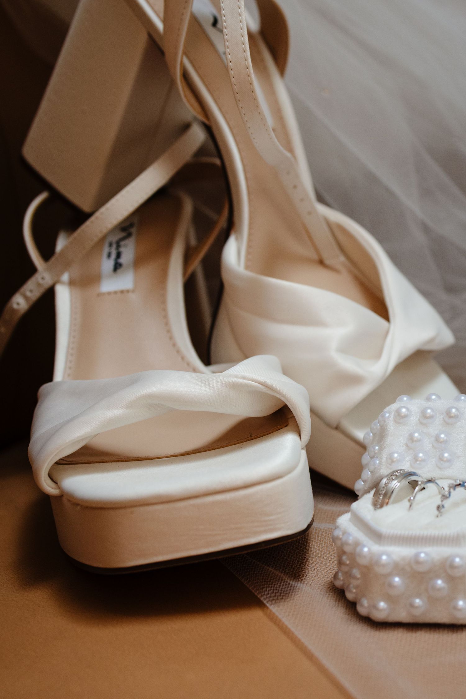 Elegant white bridal shoes with pearls and platform heels photographed in warm light.