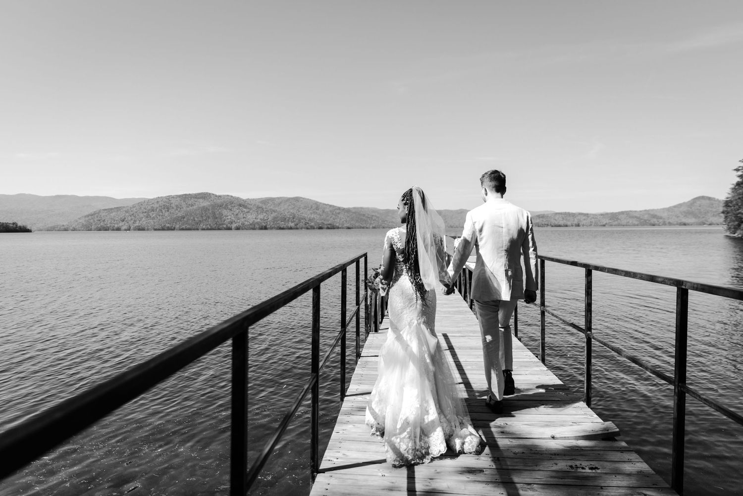 A couple walks along a dock over a serene lake during their wedding day.