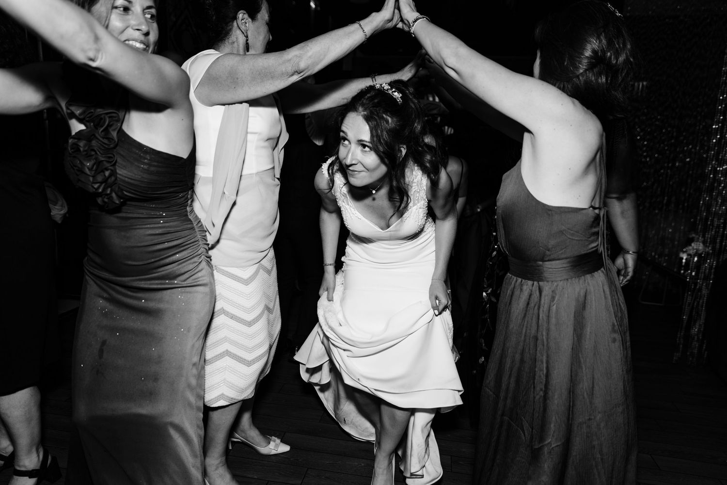 Black and white photo of wedding guests dancing and forming a circle on the dance floor.