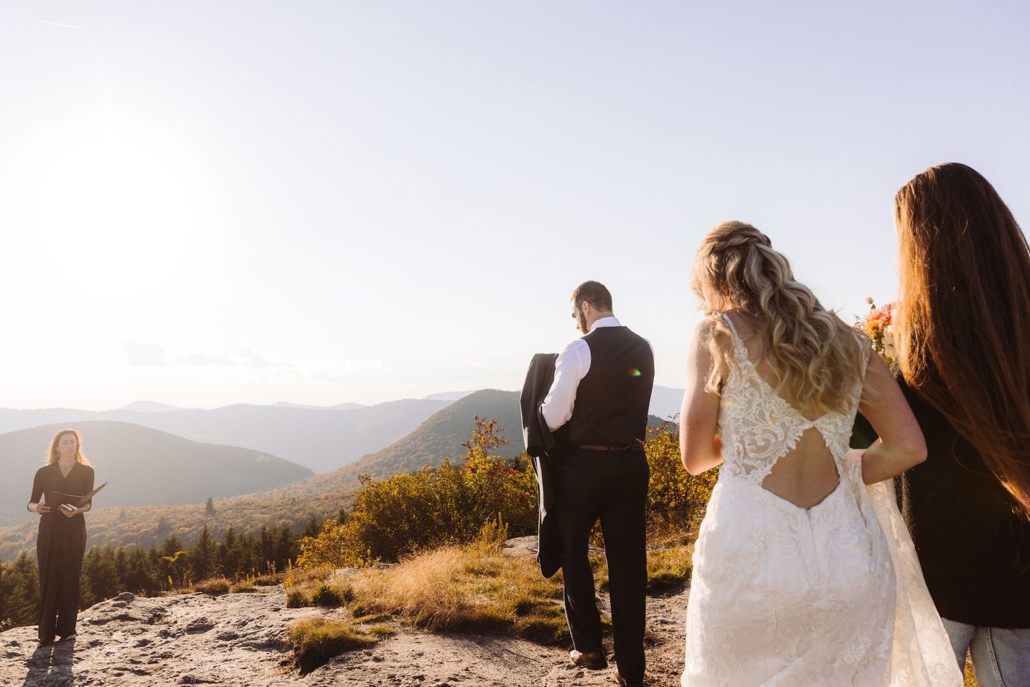 Wedding party gathered on mountaintop overlook during golden hour celebration.