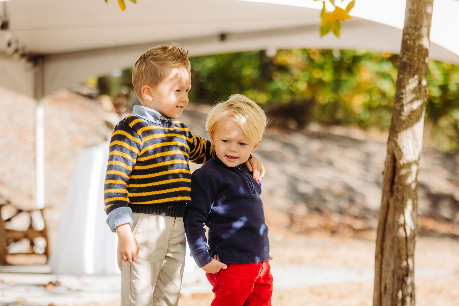 Young children playing and running outside under tall trees in natural lighting.