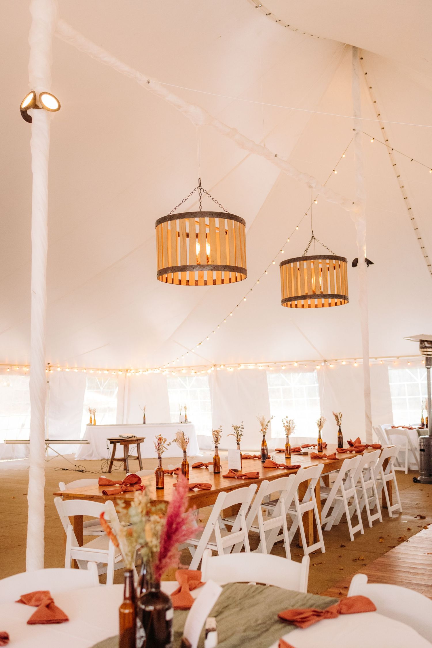 An elegant wedding reception setup with hanging drum pendant lights and white folding chairs.