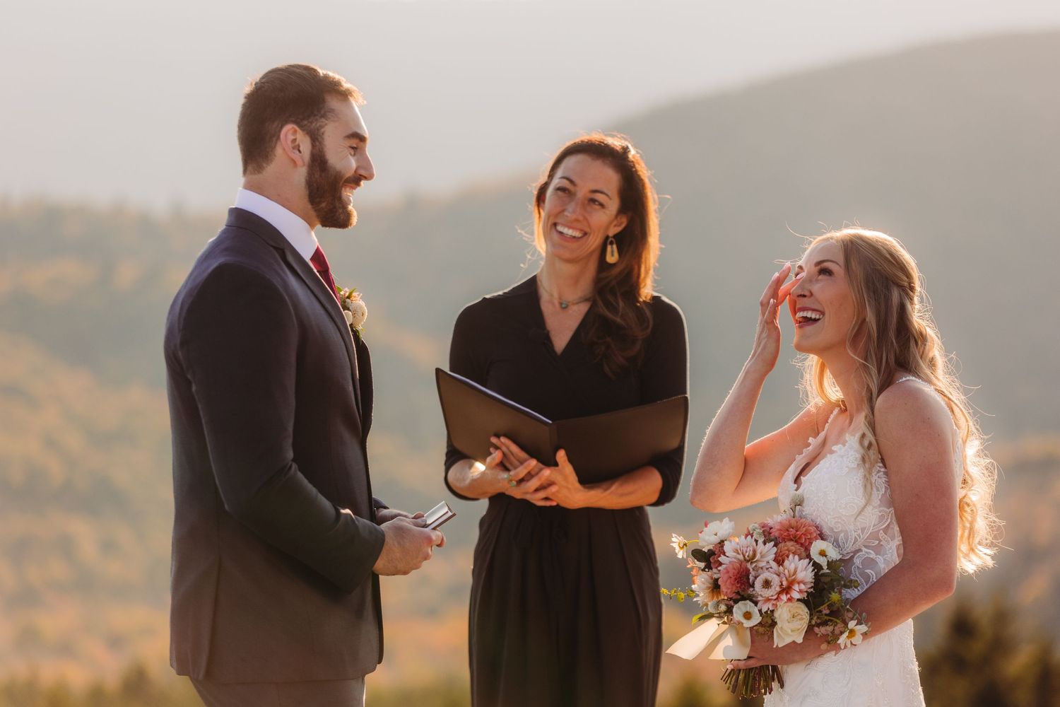 A wedding ceremony takes place on a mountaintop at golden hour with stunning fall foliage in the background.