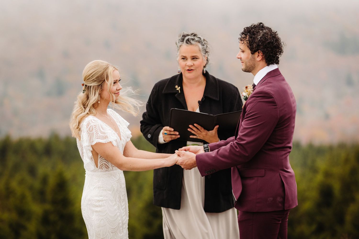 Outdoor mountain wedding ceremony with officiant in burgundy and white attire.
