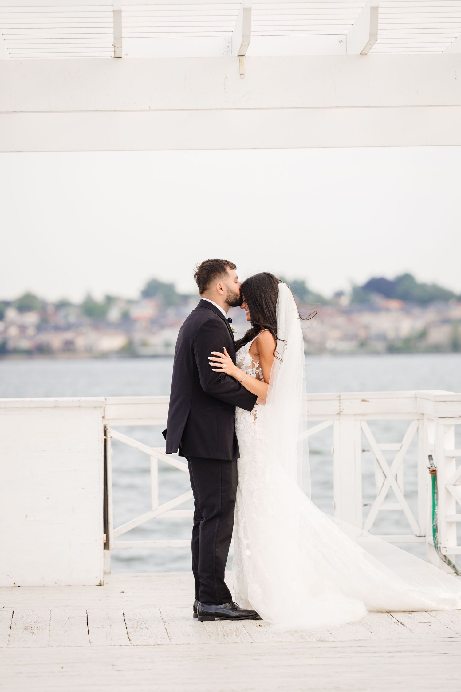 Romantic wedding moments captured on a sunlit white pier with waterfront views.