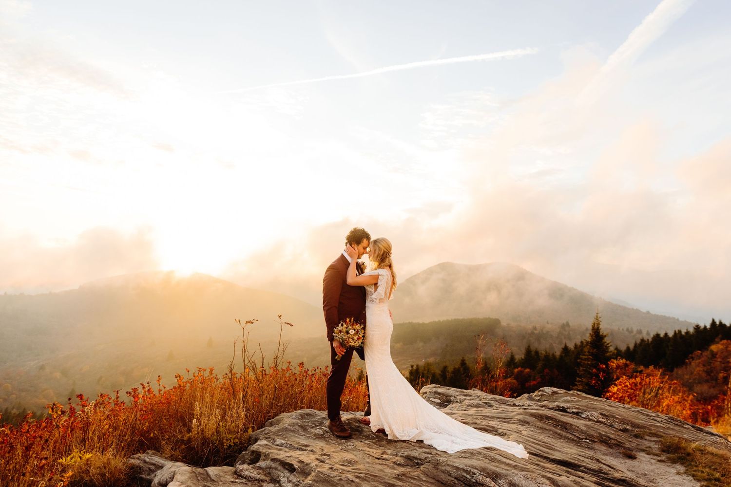 Couple shares romantic moment at sunset on mountain peak with dramatic sky backdrop.
