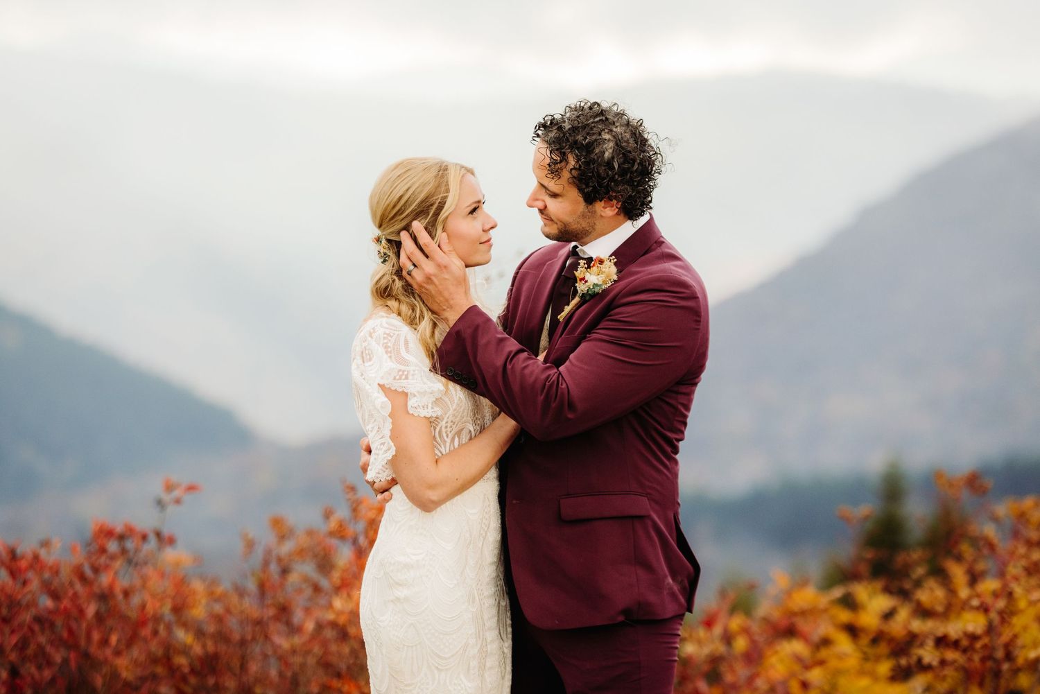 Intimate wedding moment captured against backdrop of misty mountains and burgundy fall foliage.