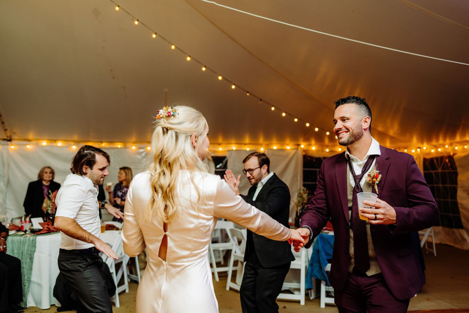Wedding celebration with dancing couples under tent lighting.