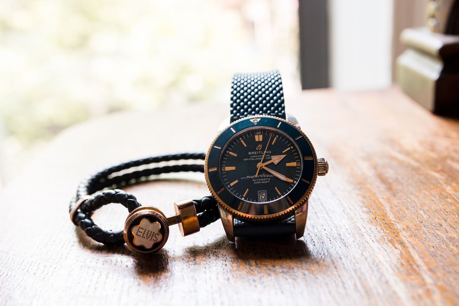 Stylish blue watch and braided leather bracelet arranged on wooden surface.