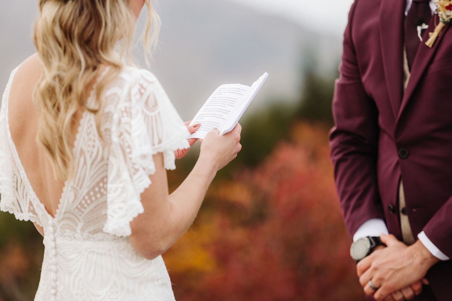 Two people share wedding vows with autumn foliage and mountains in the background.