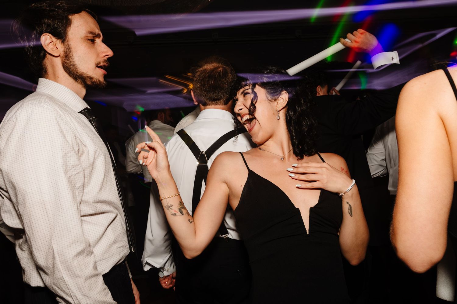 Wedding reception dance party showing energetic crowd dancing with raised arms under purple lighting.