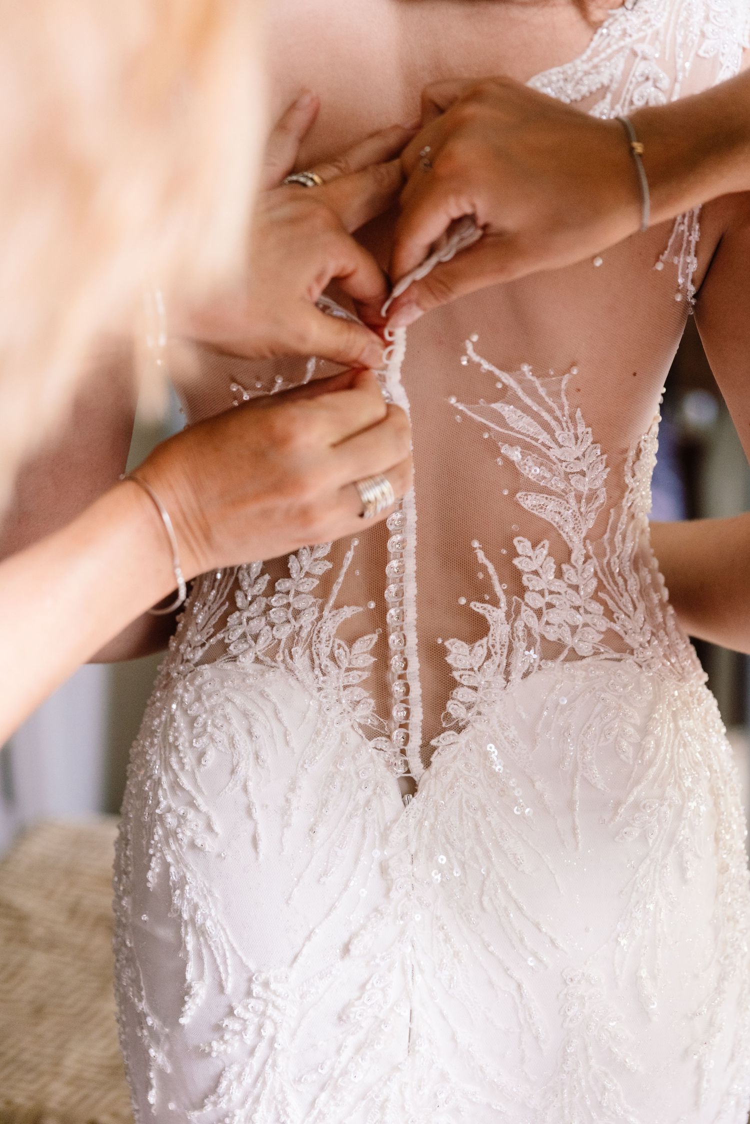 Close-up detail of intricate lace buttons being fastened on the back of a wedding dress.