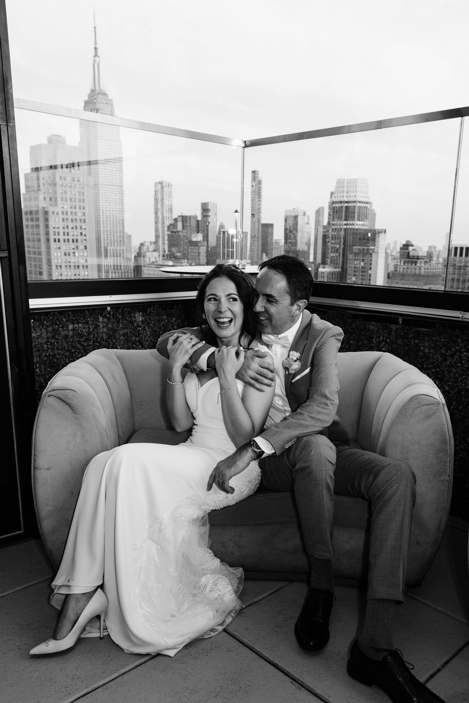 Black and white candid wedding photo with Empire State Building visible through window.