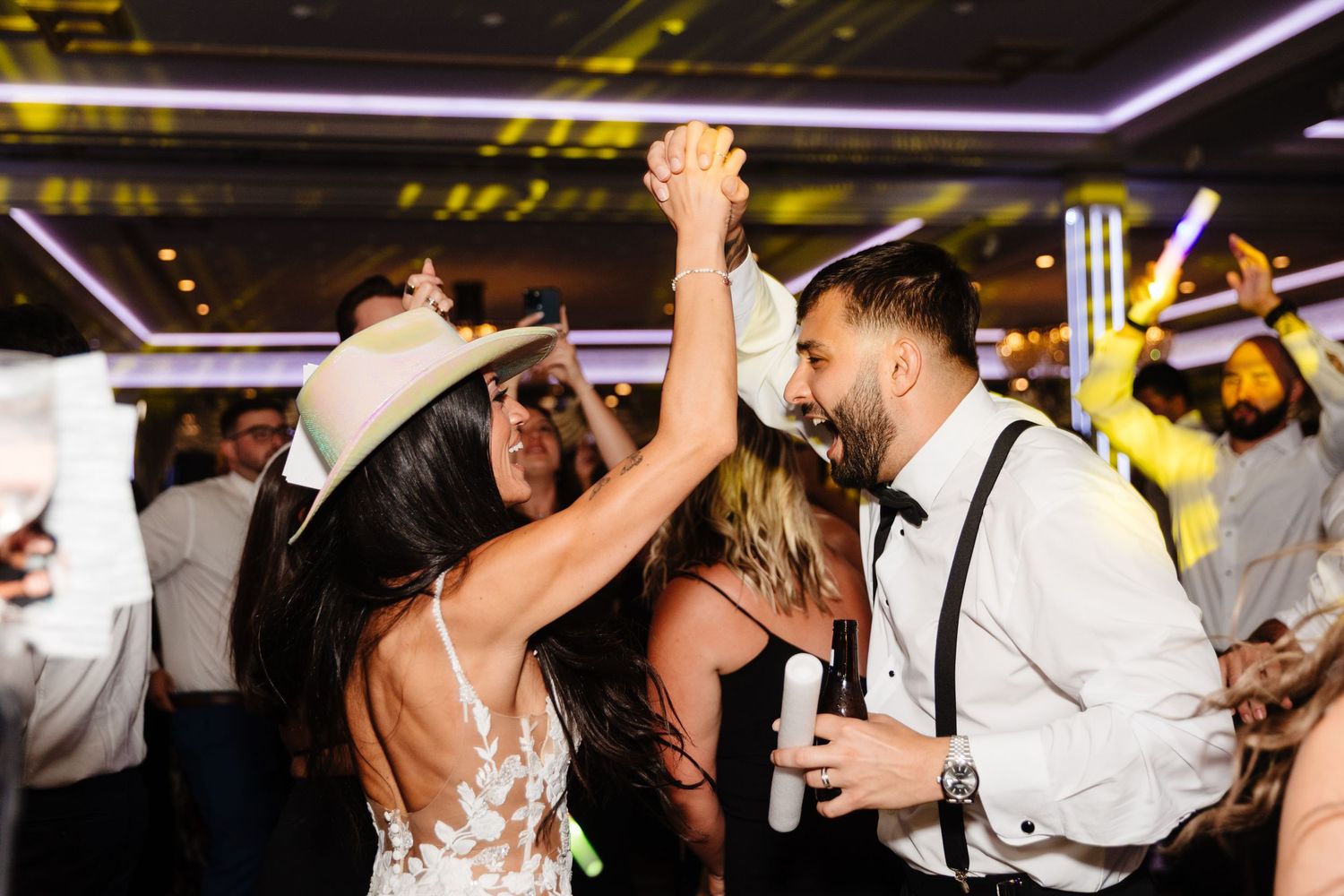 Wedding celebration with guests dancing under dramatic purple and yellow lighting.