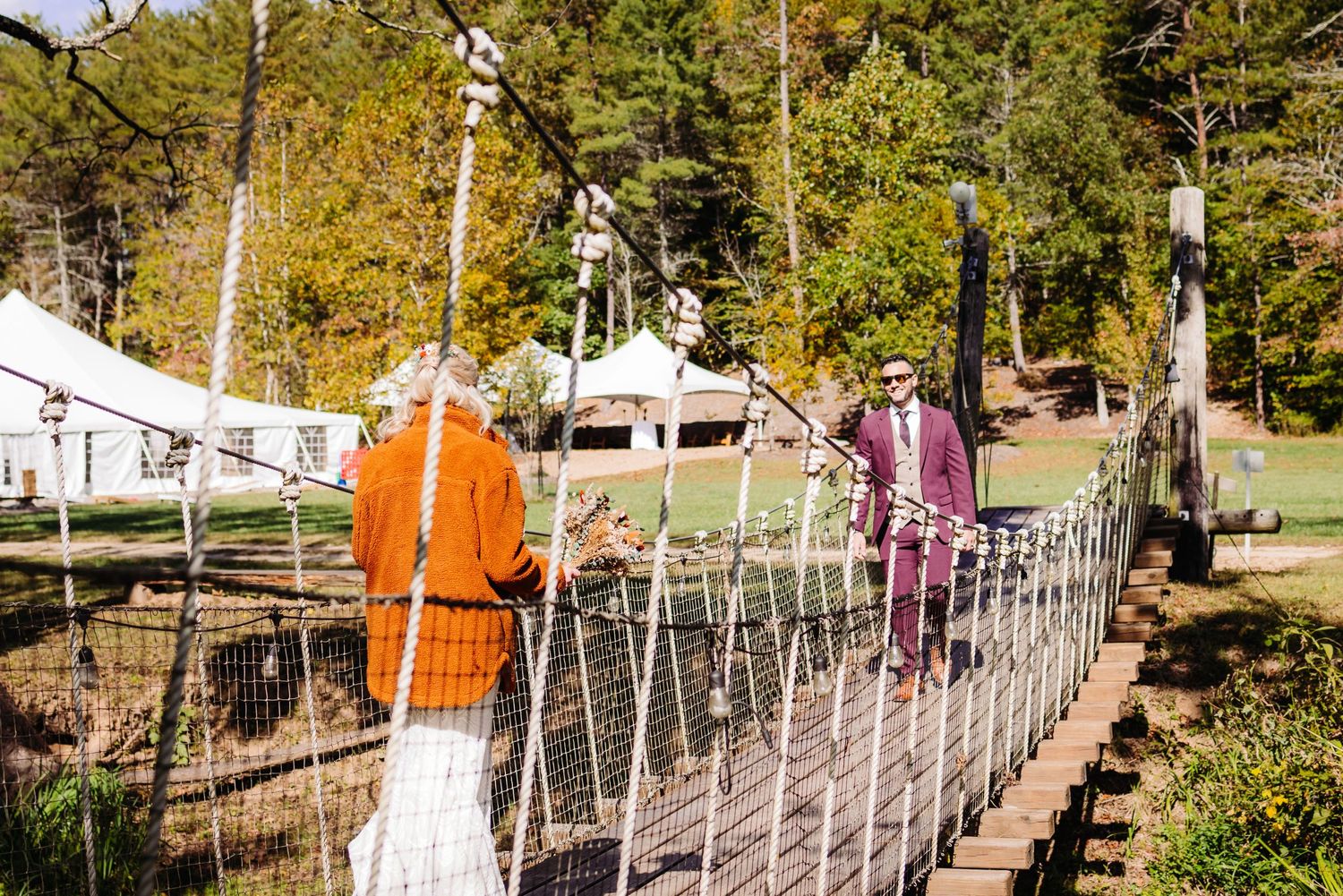 A rope bridge walkway stretches across an outdoor adventure course with fall foliage in the background.