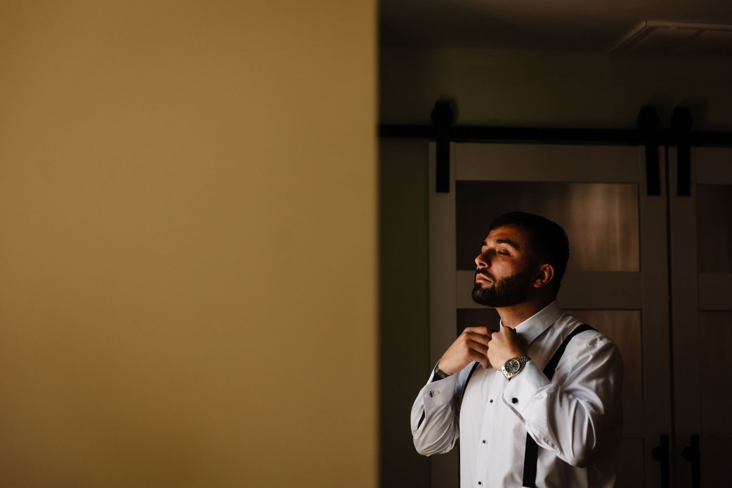 Groom in formal attire prepares for wedding day in sepia-toned lighting.