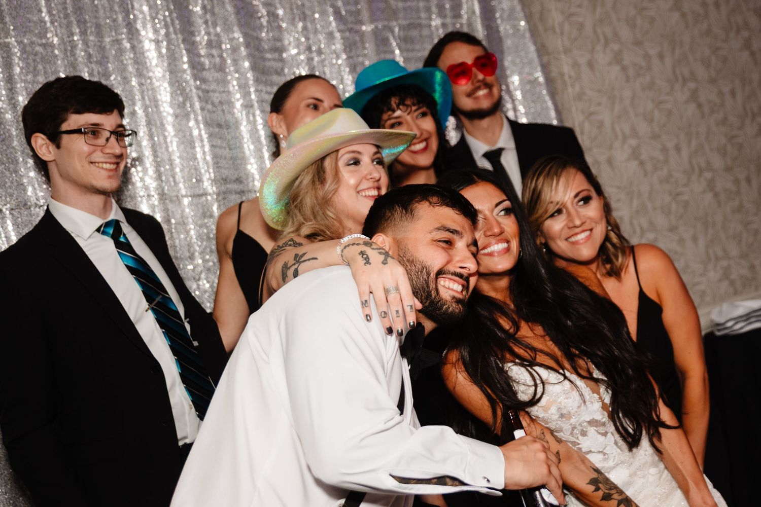 Wedding party poses together for a fun group photo against a sparkly backdrop.