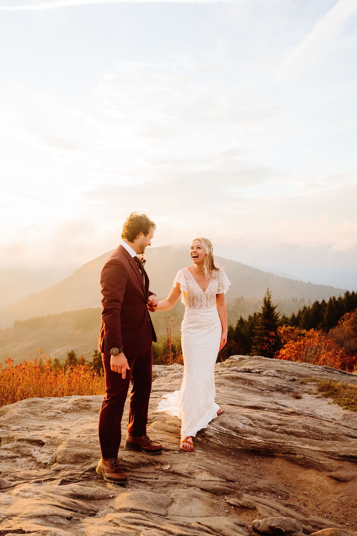 A joyful moment between newlyweds on a rocky mountain ledge at sunset.