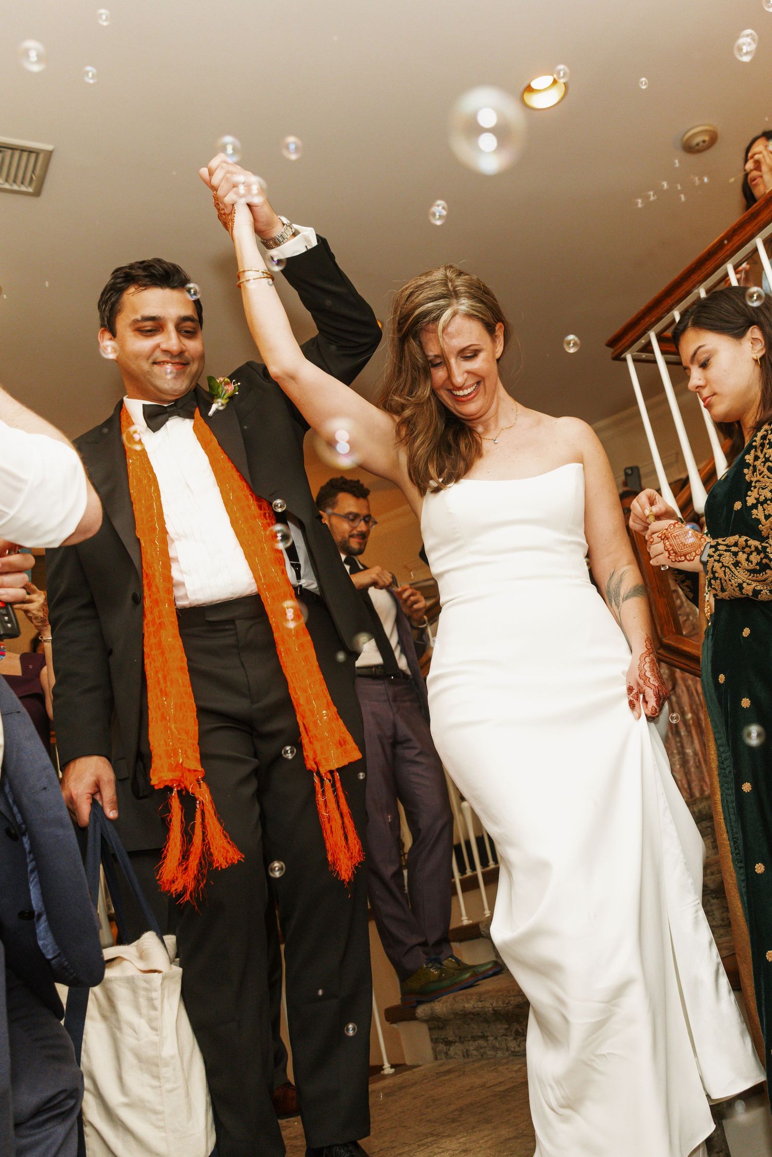A wedding celebration scene with people dancing and having fun while wearing orange scarves at an indoor reception.