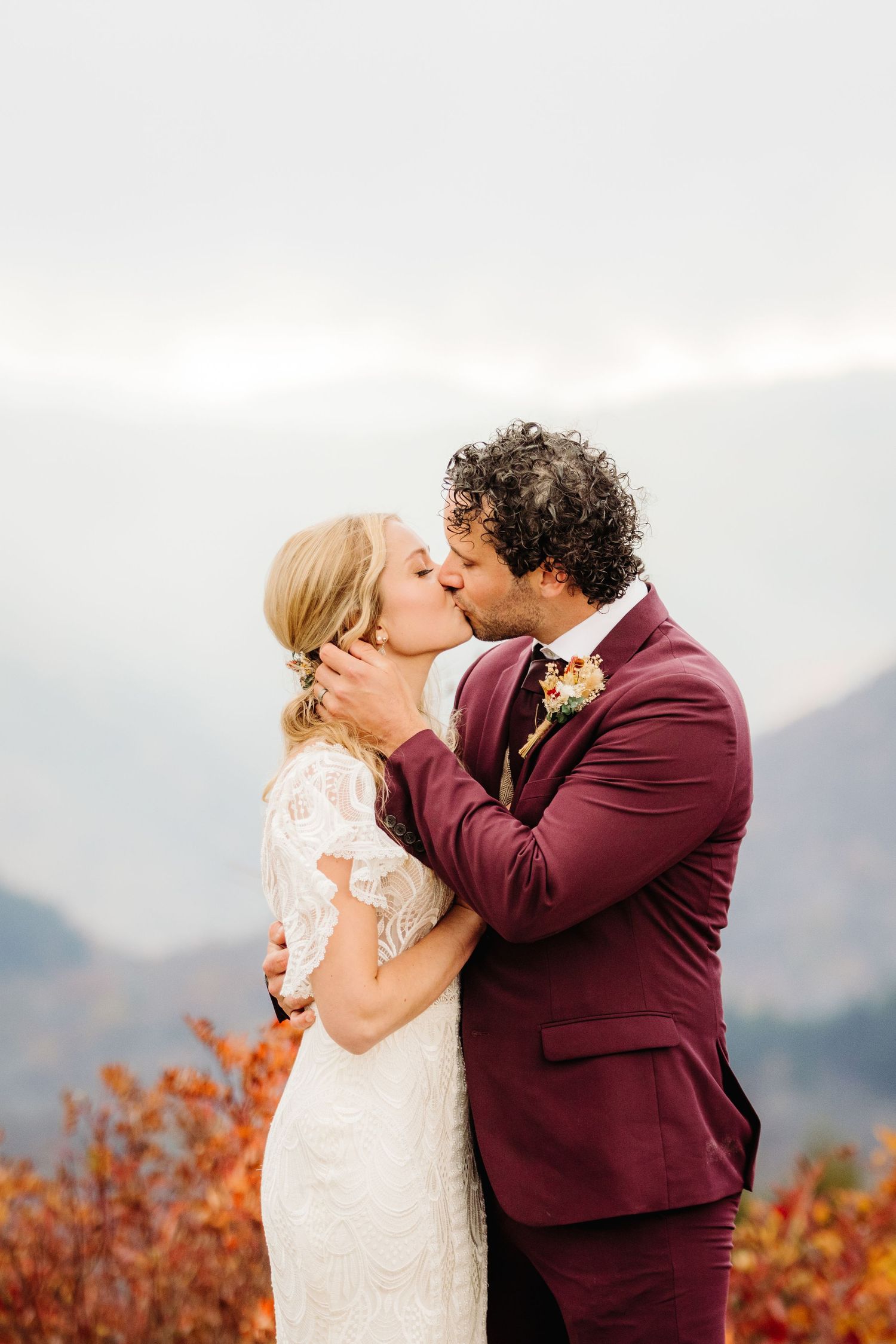 Tender wedding kiss captured against misty mountain backdrop with fall colors.