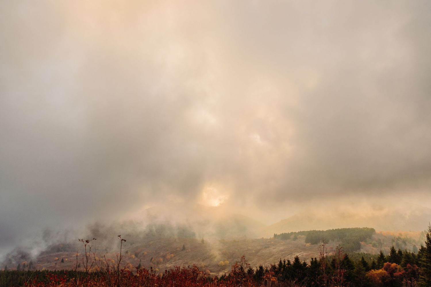 Dramatic sunset sky with misty mountains and autumn foliage beneath stormy clouds.