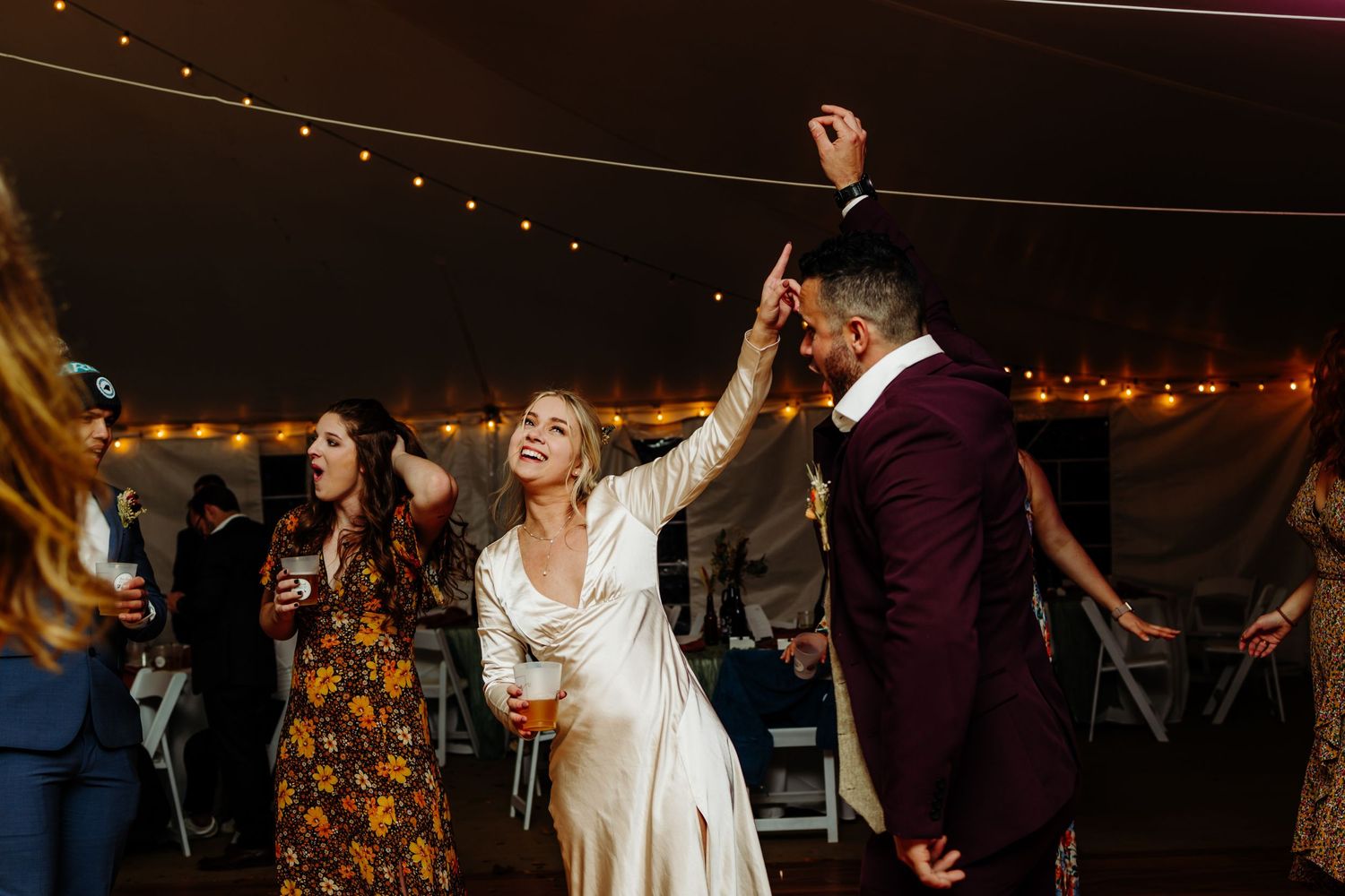 Wedding celebration on dance floor with guests under string lights in festive atmosphere.