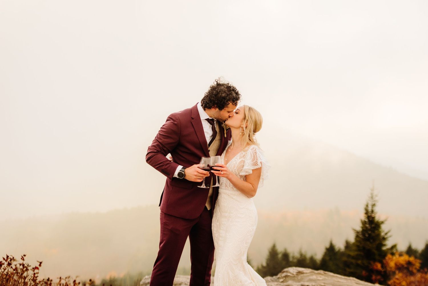 Couple embraces against misty mountain backdrop during sunset wedding ceremony.