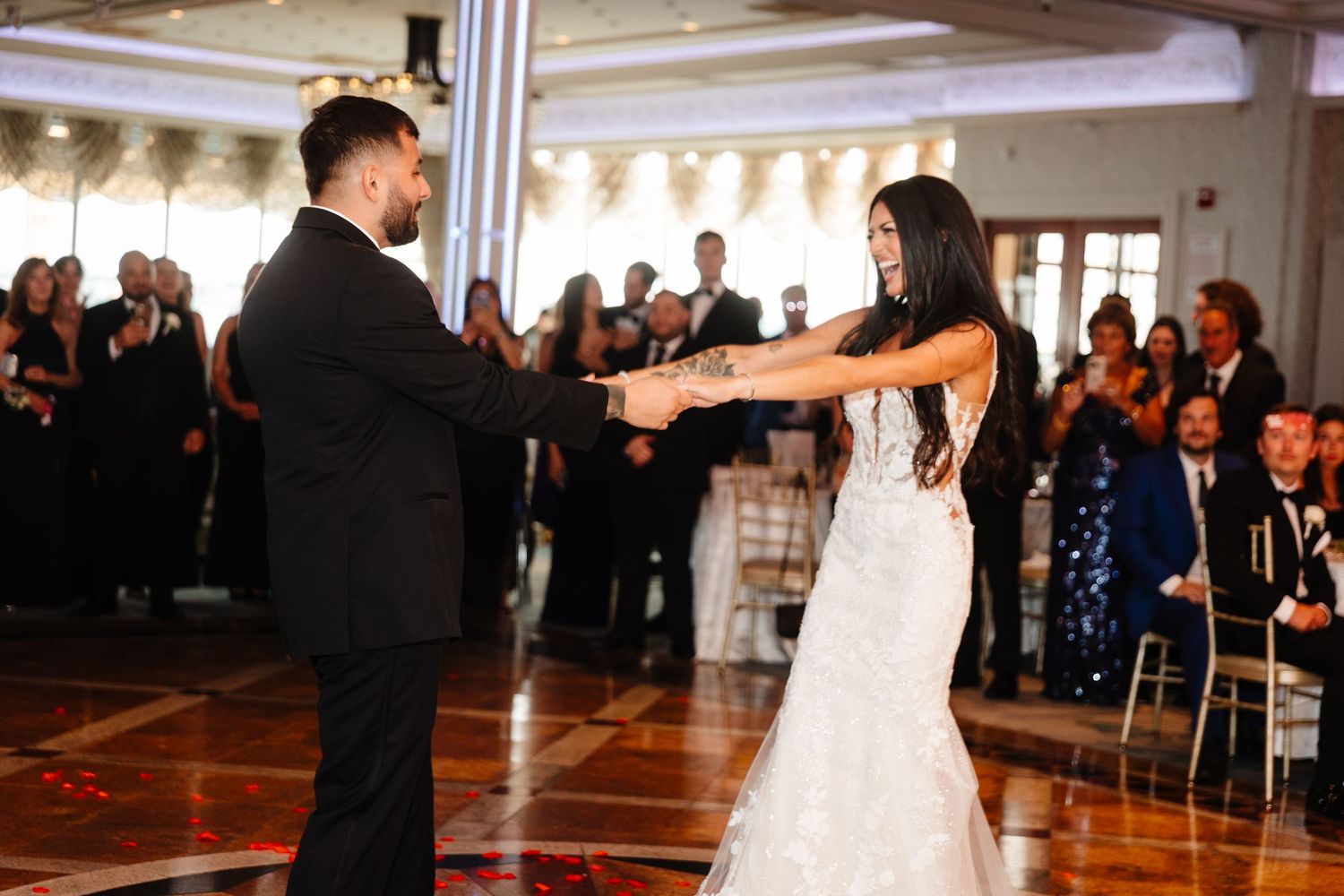 Newlyweds share their first dance on an elegant ballroom floor surrounded by wedding guests.
