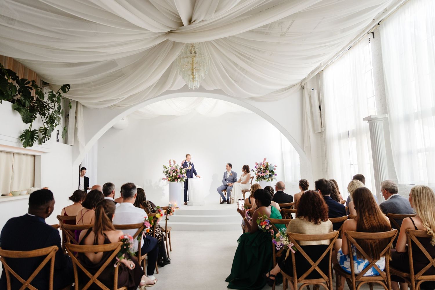 Wedding guests seated in wooden chairs under a draped white tent ceiling during the ceremony.