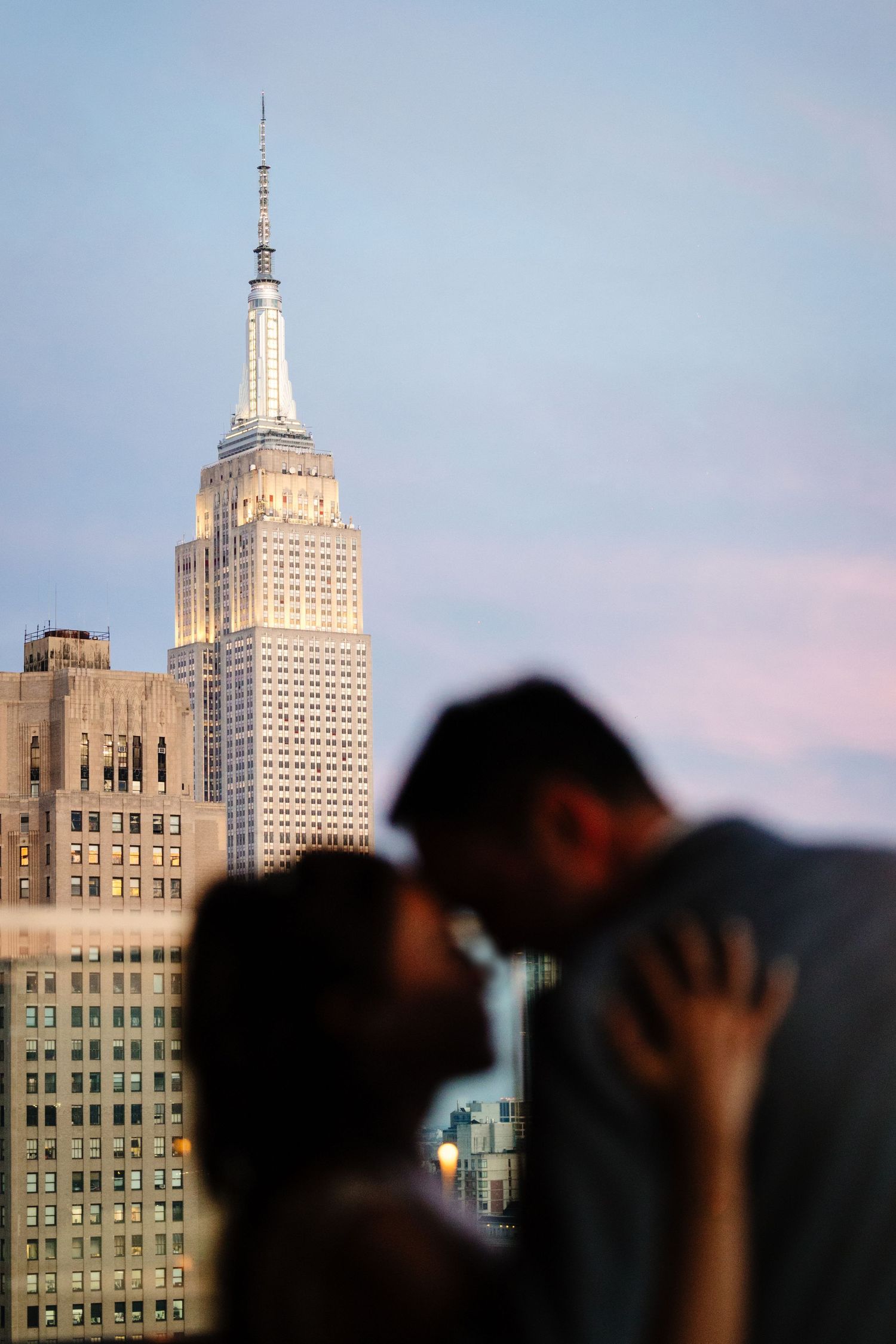 Silhouetted people viewing the Empire State Building and New York City skyline at dusk.