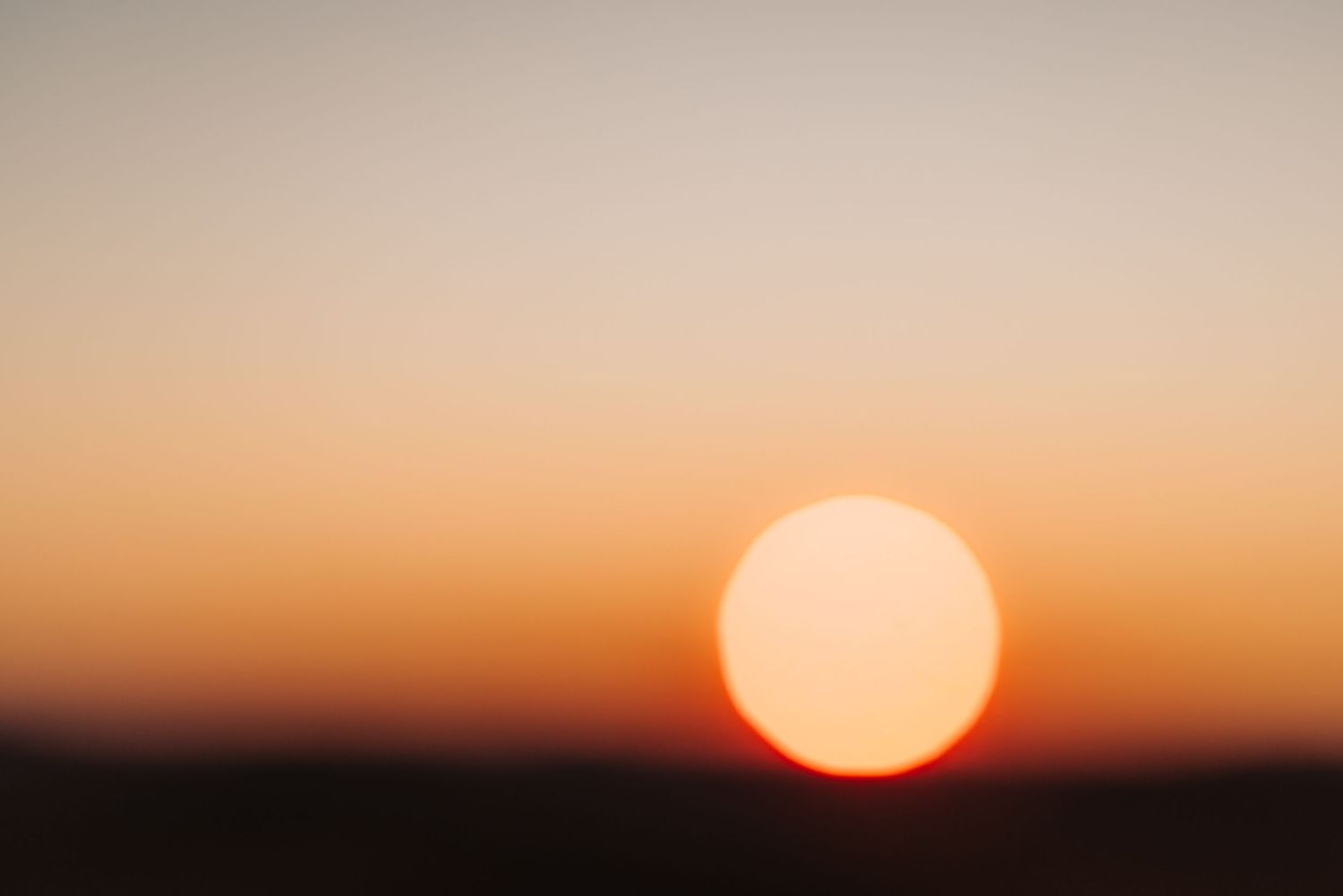 A bright orange sun glows in a gradient sky during sunset.