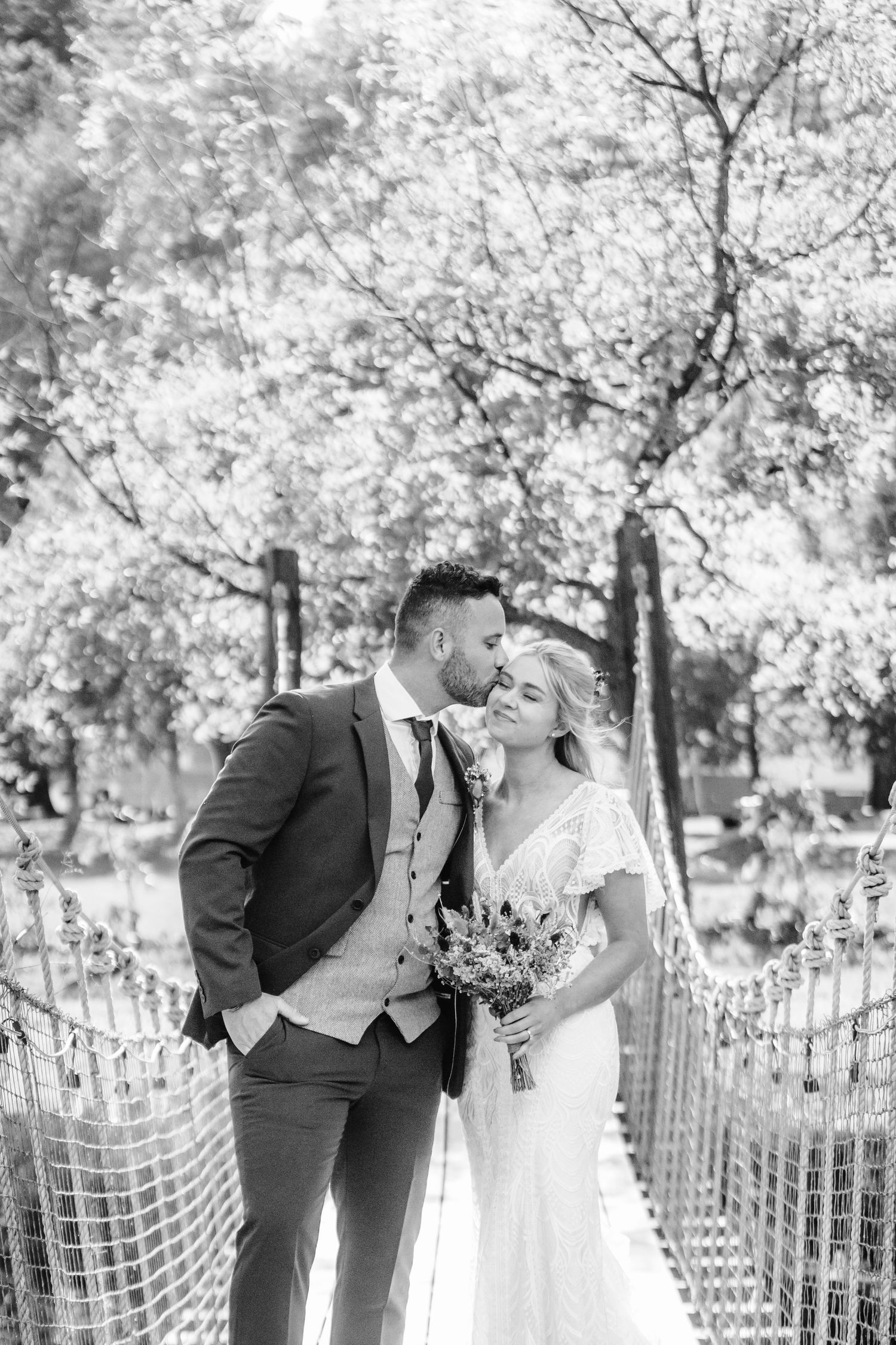 A romantic moment on a rope bridge surrounded by autumn trees in black and white.