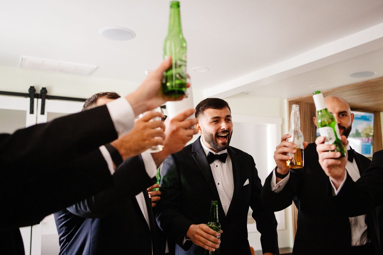 Groomsmen raise beer bottles in celebration during pre-wedding preparations.