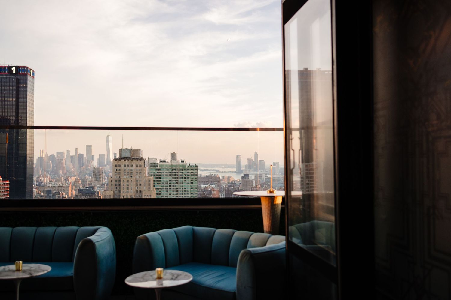 Luxury lounge area with blue velvet seating overlooking city skyline at sunset.