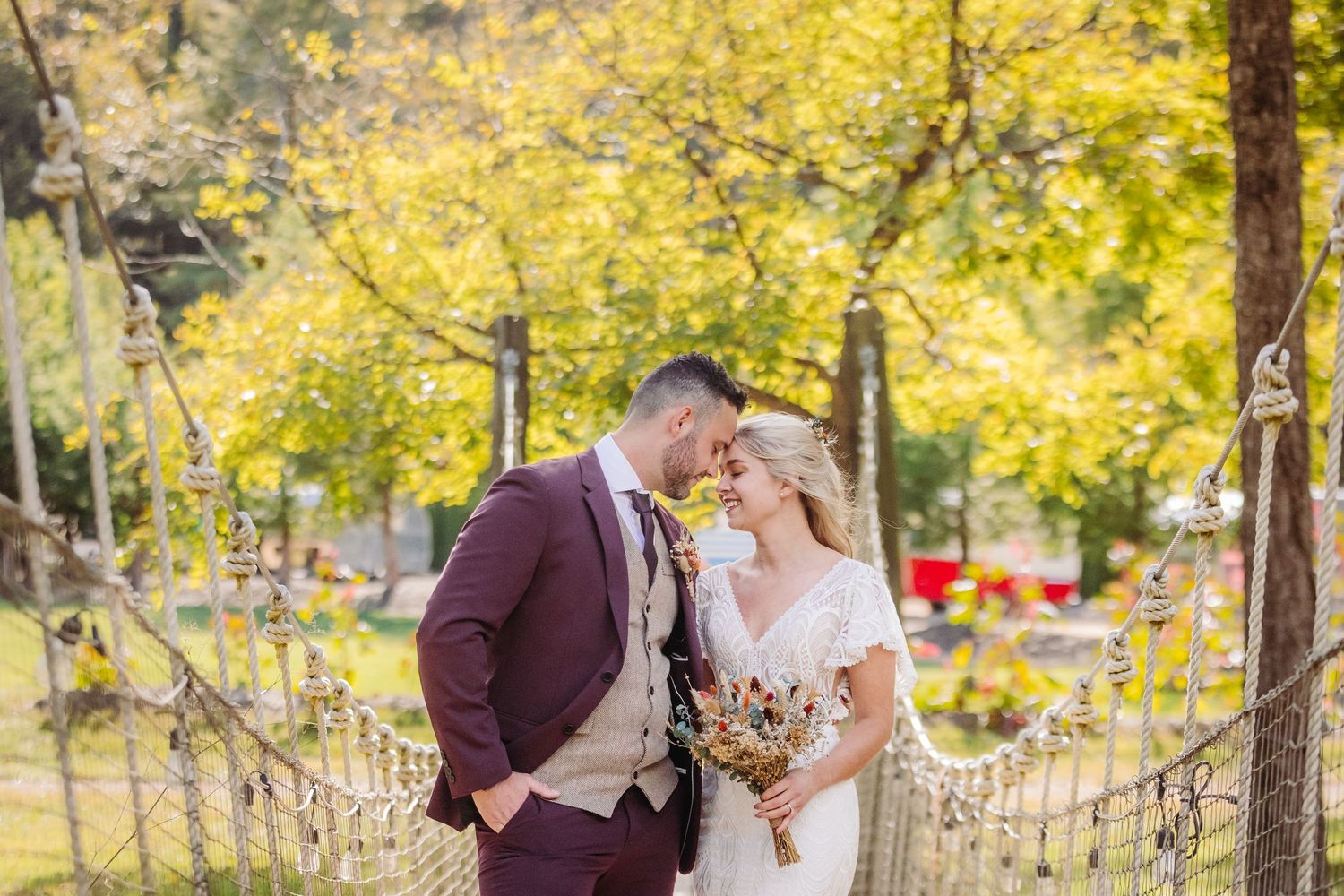A couple shares a romantic moment on a suspension bridge surrounded by autumn foliage in golden light.