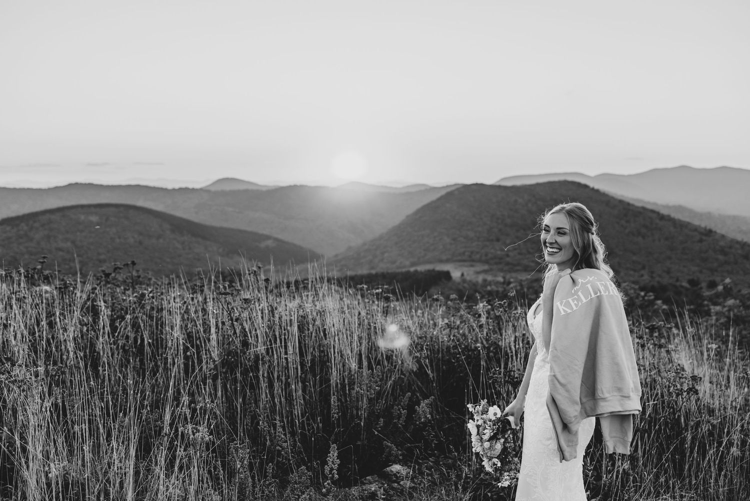 Black and white wedding portrait with sweeping mountain views and tall grass in foreground.
