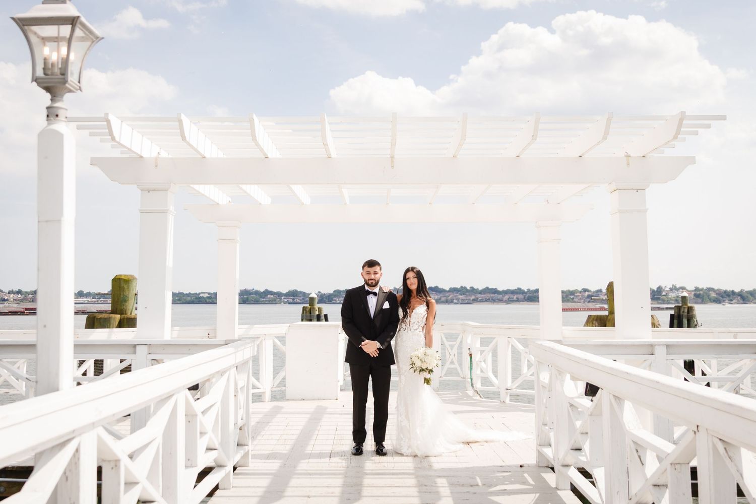 Panoramic view of coastal wedding venue with white pergola and waterfront backdrop.