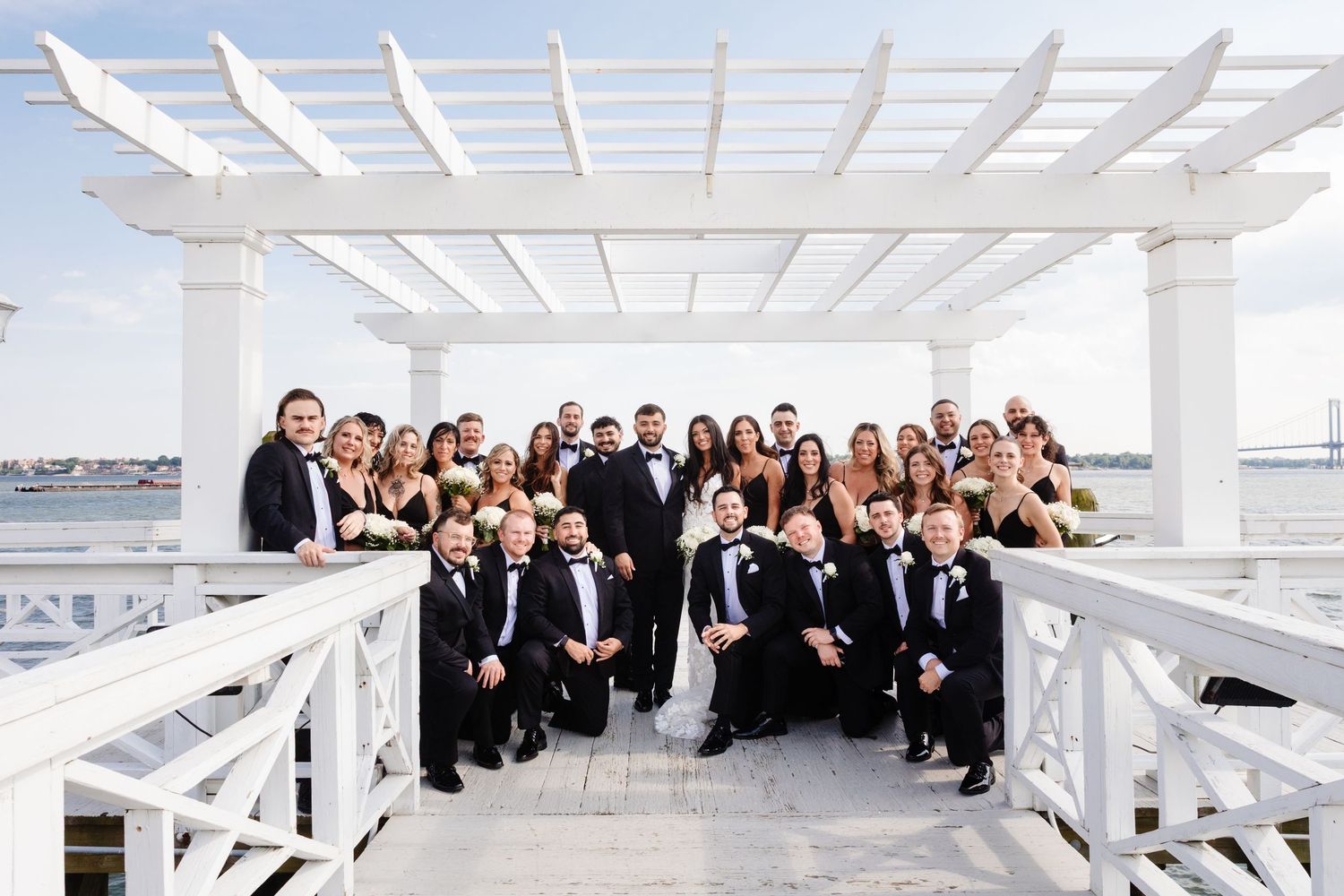 Wedding party poses creatively under a white pergola structure.