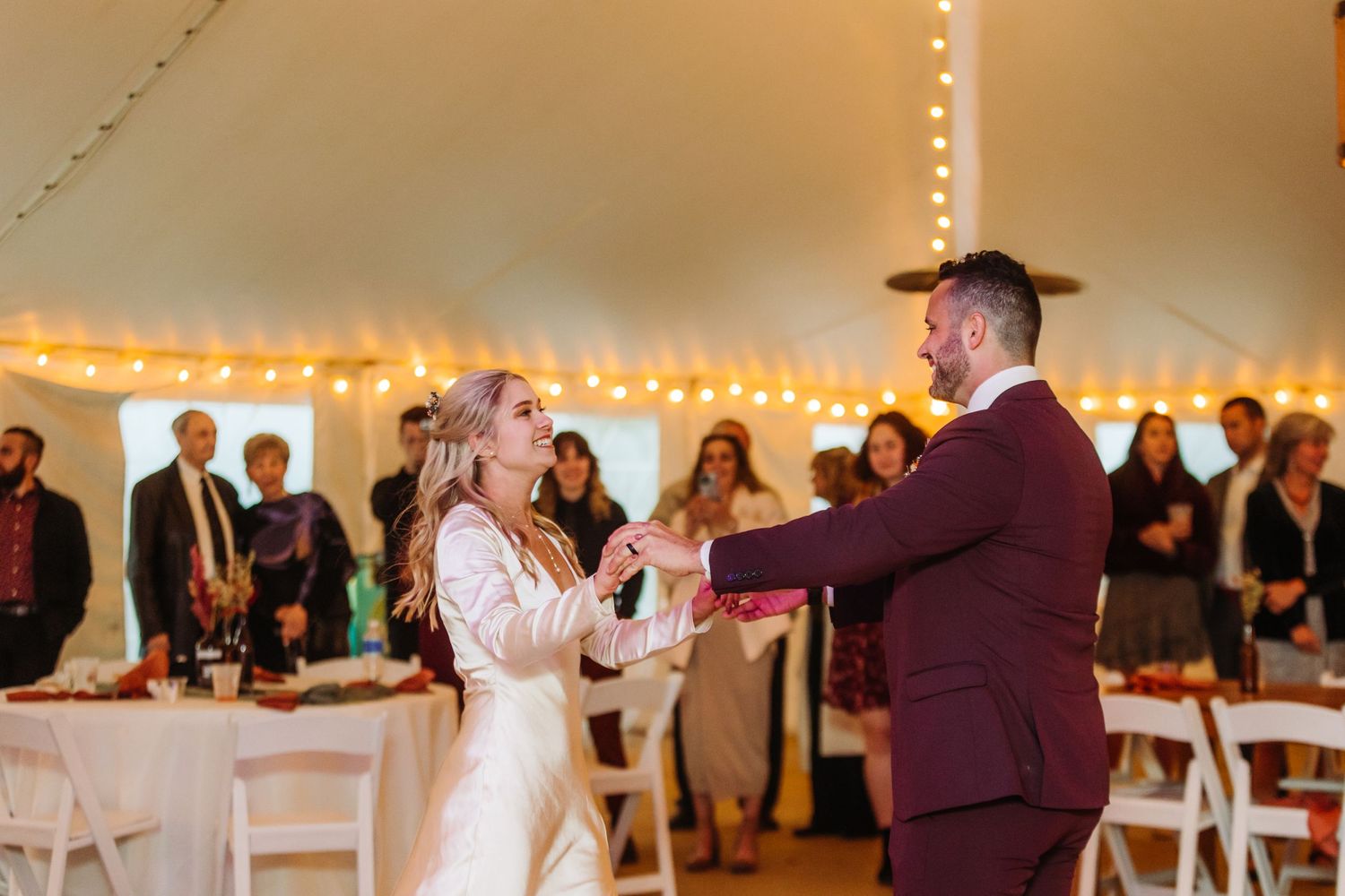 Newlyweds dance together under string lights in wedding tent.