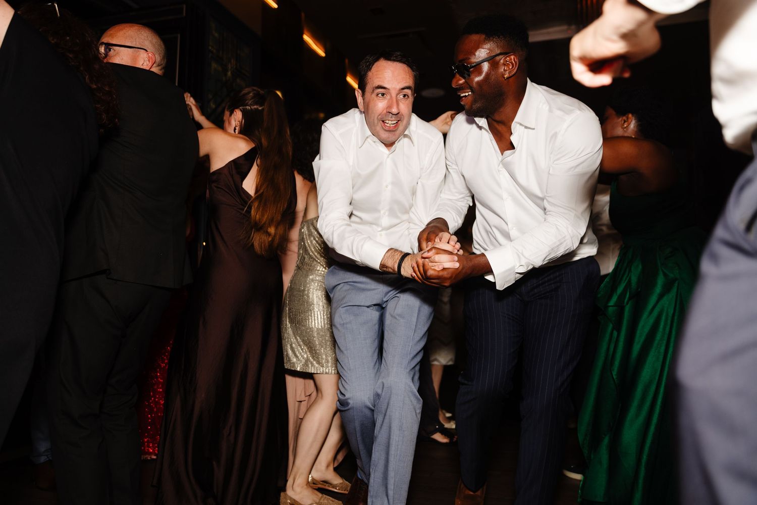 Wedding guests dancing enthusiastically at a dimly lit reception.