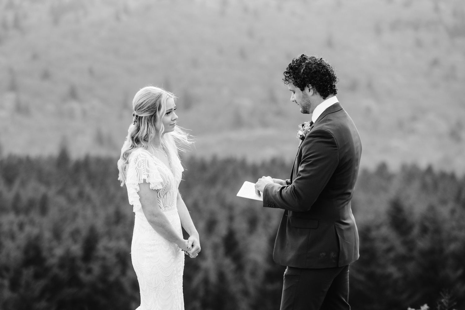 A black and white wedding ceremony moment on a mountaintop with a stunning forested valley backdrop.