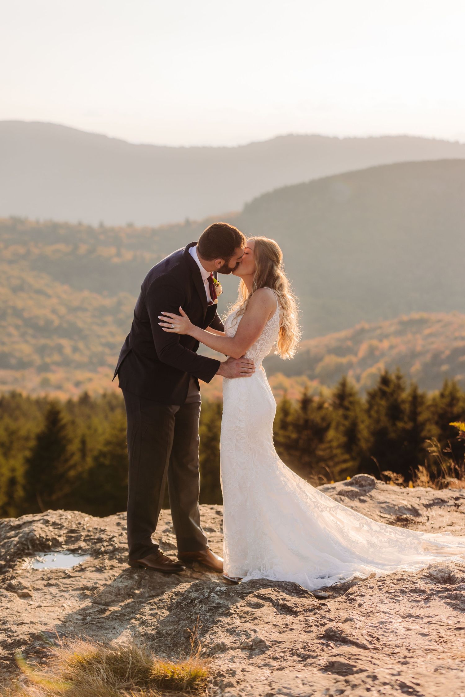 Romantic wedding couple embraces on mountain cliff during sunset with scenic valley views.