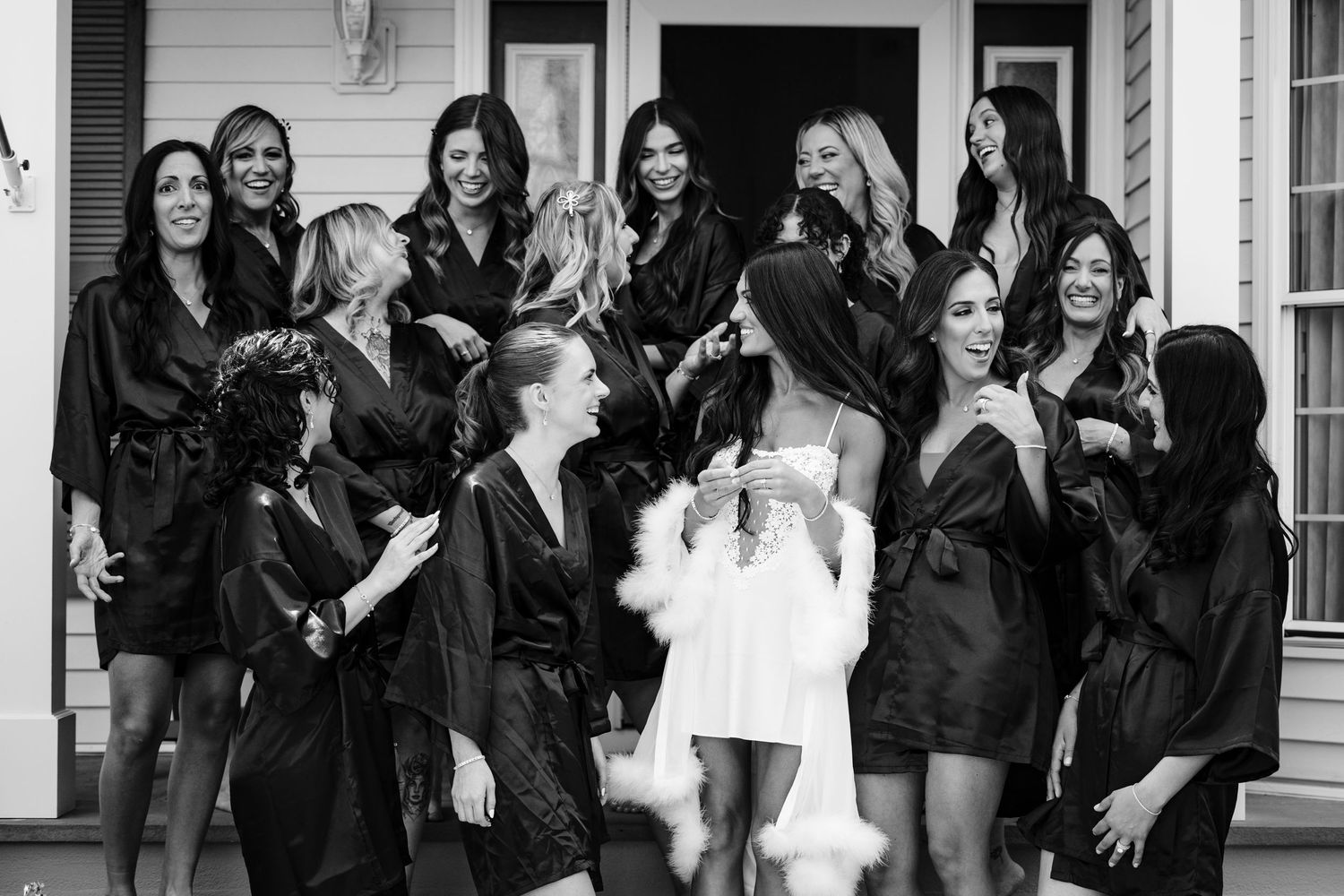Group in matching black robes gathered on porch steps for pre-wedding celebration.
